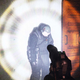 A robot in a dark room stands motionless in the glow of a large flashlight.